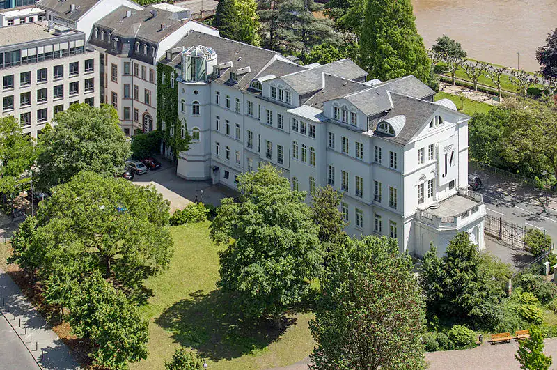 frankfurt-juedisches-museum-nordseite Luftaufnahme des Liebieghauses in Frankfurt, Deutschland. Das historische weiße Gebäude mit Schieferdach ist von Bäumen und Grünflächen umgeben und liegt eingebettet im berühmten Museumsuferviertel. Im Hintergrund sind der Main und andere Gebäude in der Nähe zu sehen.