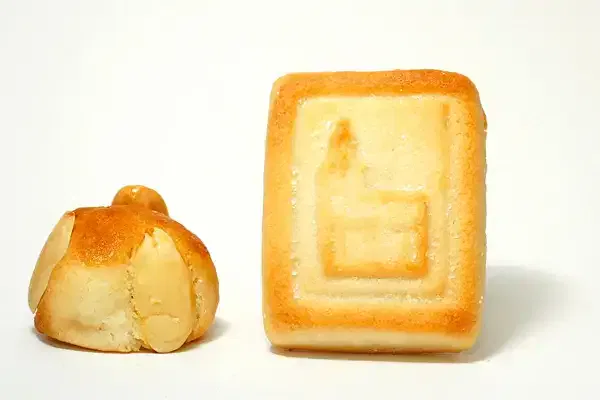 Das Bild zeigt zwei Backwaren. Links ist ein kleines rundes Gebäck mit Mandeln belegt, rechts ist ein rechteckiges Gebäck mit einem geprägten Muster auf der Oberseite. Der Hintergrund ist schlicht weiß.