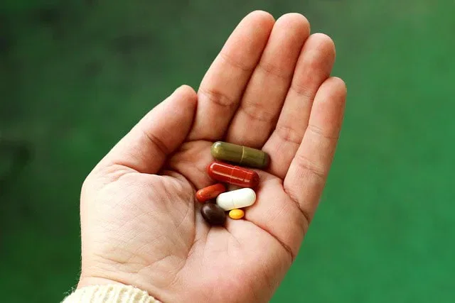 Eine Hand hält mehrere sortierte, beliebte Nahrungsergänzungsmittel - Pillen und Kapseln in verschiedenen Formen, Größen und Farben - vor einem unscharfen grünen Hintergrund.
