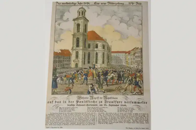 paulskirche-bilderrevolution-2 Eine Illustration eines historischen Ereignisses, die eine große Menschenmenge zeigt, die sich vor der Paulskirche mit ihrem hohen Glockenturm versammelt hat. Die Szene ist lebendig, mit Menschen, die verschiedenen Aktivitäten nachgehen. Der deutsche Text unter dem Bild beschreibt die Szene als Teil eines bemerkenswerten Ereignisses im Jahr 1848.