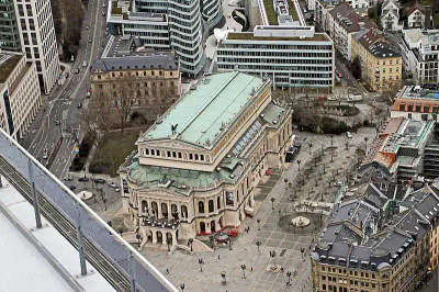 Luftaufnahme des Gebäudes Alte Oper in Frankfurt, Deutschland. Die historische Alte Oper ist von modernen und traditionellen Gebäuden umgeben, mit von Bäumen gesäumten Straßen und Fußgängern. Der Platz vor dem Opernhaus weist einen symmetrischen Grundriss auf.