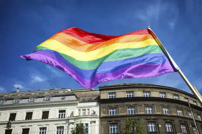 Eine Regenbogenfahne, die den LGBTQ+-Stolz symbolisiert, weht während der Festtage vor einem blauen Himmel. Die Flagge wird über historischen Gebäuden gehisst und demonstriert Stärke und Einheit innerhalb der LGBTQ+-Community.
