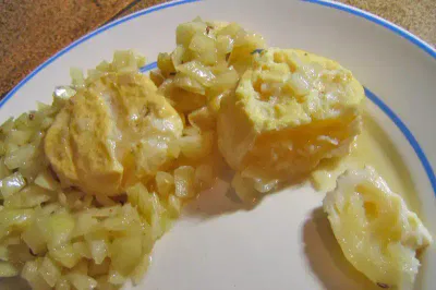 Ein Teller mit Rührei und sautierten Zwiebeln. Die Eier sind locker und goldfarben, während die Zwiebeln karamellisiert und durchscheinend sind, was ein wohltuendes und herzhaftes Gericht ergibt. Der Teller hat ein einfaches weiß-blaues Design.