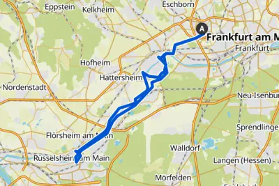 Eine Karte, die eine Route von Frankfurt am Main nach Rüsselsheim am Main, Deutschland, zeigt. Die Route ist mit einer blauen Linie markiert und verläuft durch Orte wie Kelsterbach, Hattersheim und Flörsheim am Main. Umliegende Gebiete und kleinere Städte sind auf der Karte markiert.