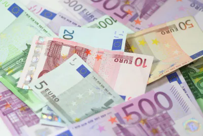 Ein verstreuter Stapel von Euro-Banknoten in verschiedenen Stückelungen, die oft mit der Verwaltung von Schulden oder dem Umgang mit Schufa-Schecks zu tun haben, zeigt bunte Motive und Sterne aus der Flagge der Europäischen Union.