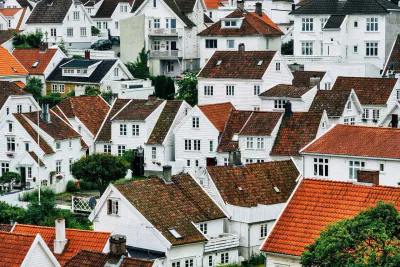 Eine Ansammlung von weißen Holzhäusern mit roten und braunen Ziegeldächern, dicht aneinander gedrängt in einer hügeligen Gegend, umgeben von Grün - eine idyllische Szene, die die Pflichten als Vermieter bei der Aufrechterhaltung solcher charmanten Gemeinden unterstreicht.