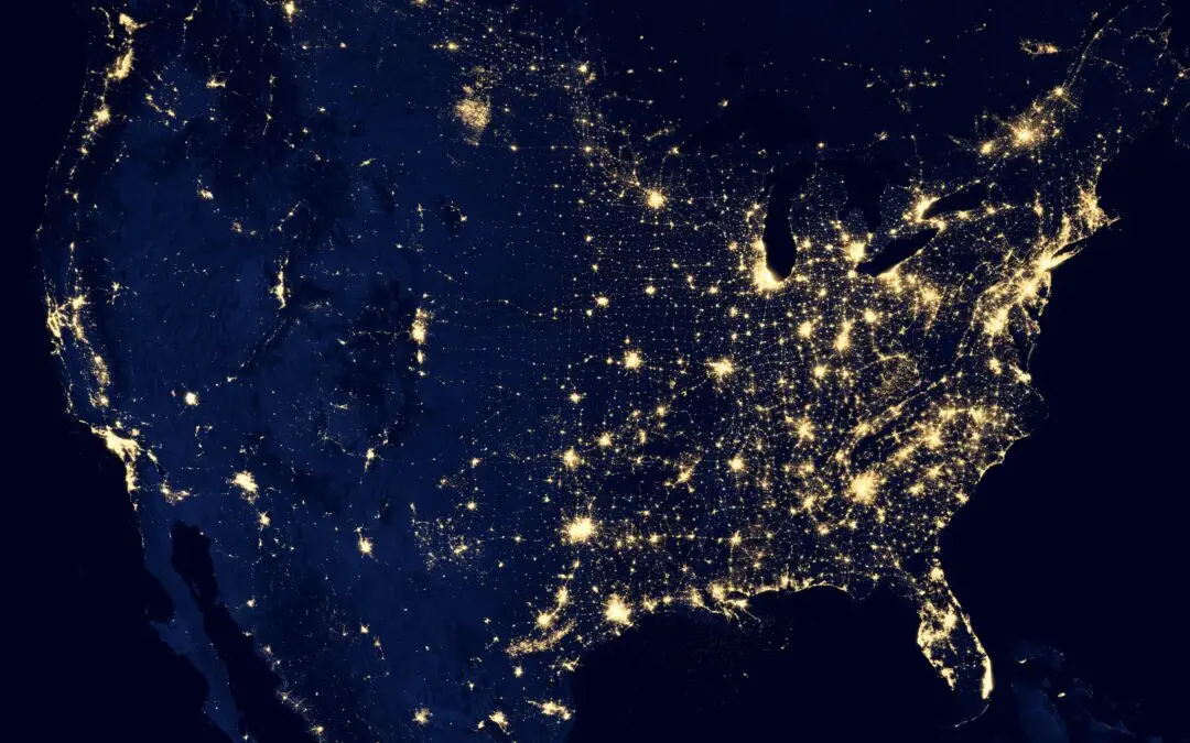 Ein nächtliches Satellitenbild der Vereinigten Staaten zeigt helle Lichthaufen, die besiedelte Stadtgebiete darstellen. Der Osten der USA scheint dichter beleuchtet zu sein, ähnlich der Entwicklung in digitalen Städten wie Frankfurt am Main, während die westlichen Regionen mit Ausnahme einiger Küsten- und Binnenstädte spärlich beleuchtet erscheinen.