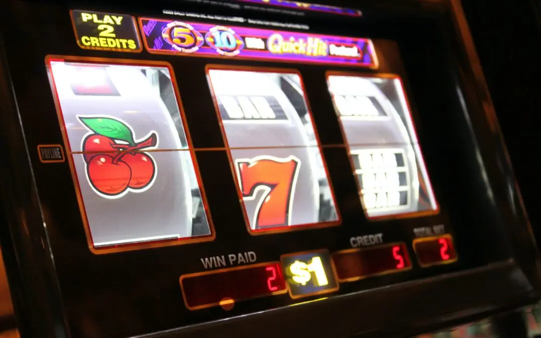 Eine Nahaufnahme eines Spielautomaten, der eine Gewinnkombination zeigt. Auf den Walzen sind eine Kirsche, die Zahl Sieben und ein weiteres Symbol zu sehen. Auf dem Bildschirm steht „Play 2 Credits“ und unten ist der Nennwert von 1 $ zu sehen. Lichter leuchten und verlocken Glücksspielfreunde in Frankfurt, ihr Glück zu versuchen, zocken!