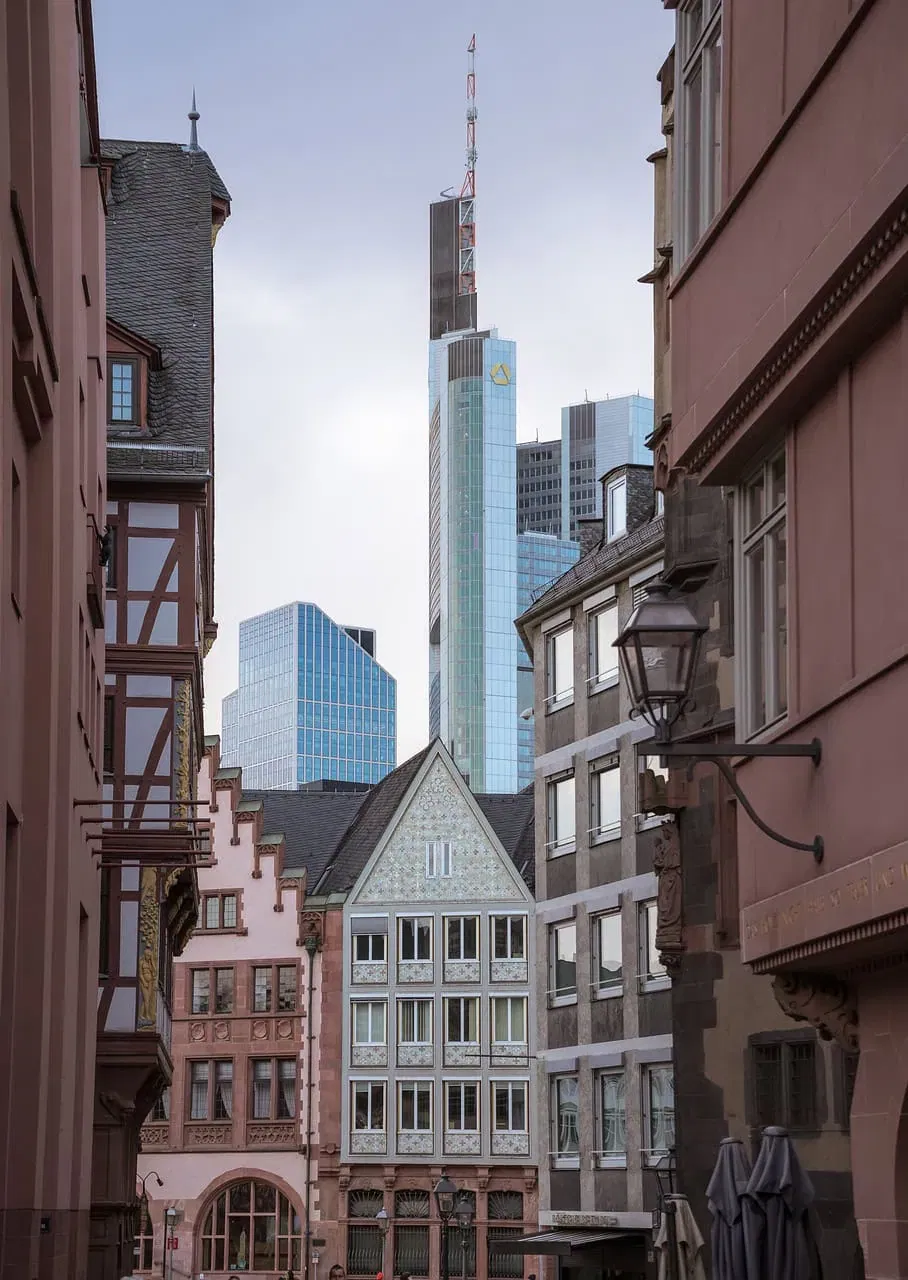 Eine schmale Straße in Frankfurt zeigt eine Mischung aus traditioneller und moderner Architektur. Fachwerkhäuser säumen den Vordergrund, während im Hintergrund elegante Wolkenkratzer, darunter der Commerzbank Tower, hervorstechen – eine perfekte Kulisse für Tipps zur Verwaltung von Eigentumswohnungen.