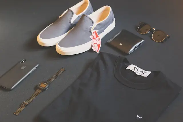 T-Shirt, Schuhe, Geldbeutel, Sonnenbrille, Armbanduhr und Handy nebeneinander gelegt.