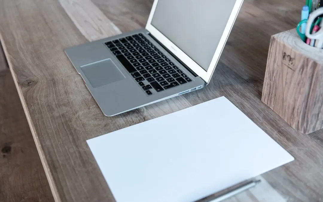 Auf einem Holzschreibtisch steht ein Laptop neben einem leeren weißen Blatt Papier, daneben ein Behälter mit Stiften und Markern – perfekt für ein Übersetzungsbüro, das Unternehmen hilft, global zu kommunizieren.